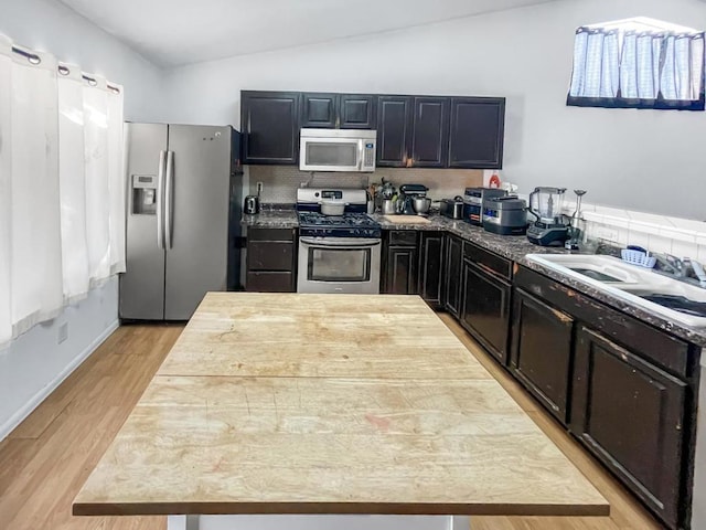 kitchen featuring sink, stainless steel appliances, light stone counters, vaulted ceiling, and light wood-type flooring