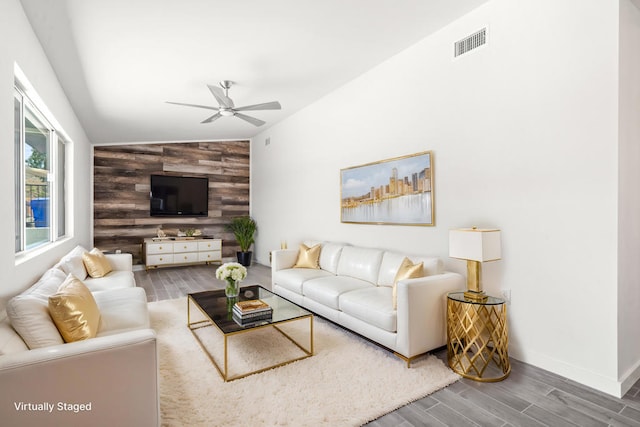 living room featuring vaulted ceiling, ceiling fan, wood-type flooring, and wood walls