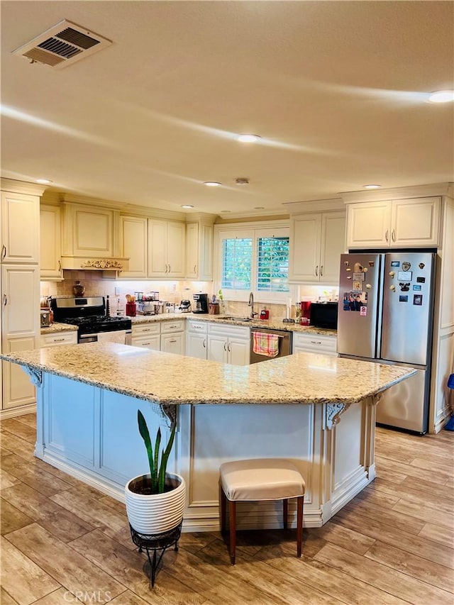 kitchen with visible vents, light stone countertops, stainless steel appliances, light wood-style floors, and a kitchen bar