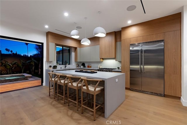 kitchen featuring a kitchen bar, a kitchen island, pendant lighting, stainless steel built in refrigerator, and sink