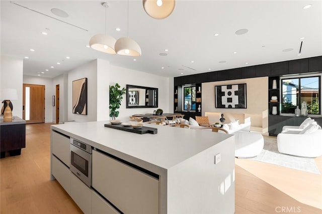 kitchen featuring decorative light fixtures, stainless steel microwave, a spacious island, white cabinetry, and light wood-type flooring