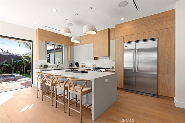 kitchen with pendant lighting, a kitchen island, stainless steel built in refrigerator, a kitchen breakfast bar, and backsplash