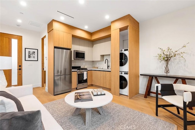 kitchen featuring stacked washer / drying machine, stainless steel appliances, decorative backsplash, sink, and light hardwood / wood-style flooring