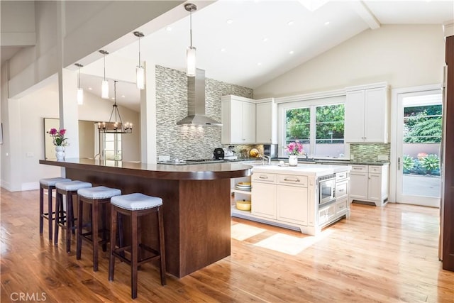 kitchen featuring stainless steel microwave, an inviting chandelier, wall chimney exhaust hood, and white cabinets