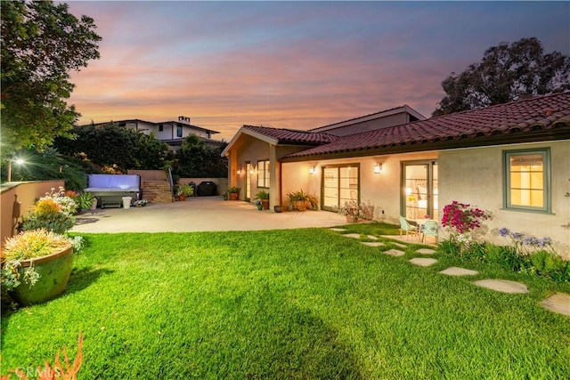 back house at dusk with a patio and a yard