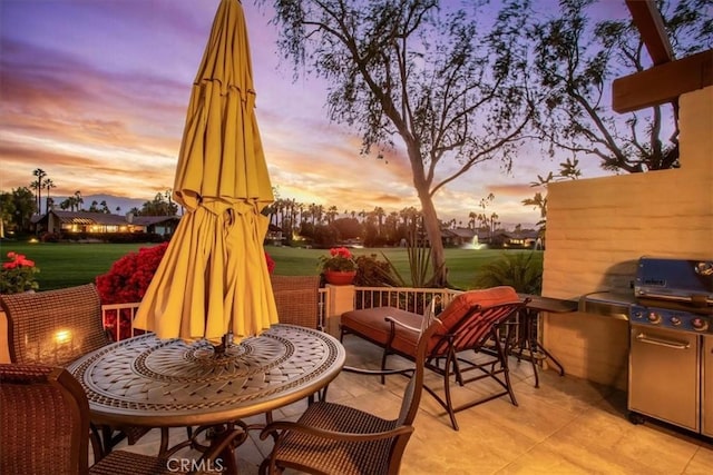 patio terrace at dusk with exterior kitchen, area for grilling, and a lawn