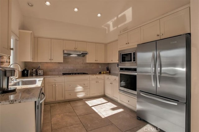 kitchen featuring appliances with stainless steel finishes, sink, white cabinets, decorative backsplash, and light stone counters