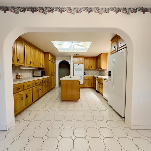 kitchen with ceiling fan, backsplash, a center island, white appliances, and a skylight