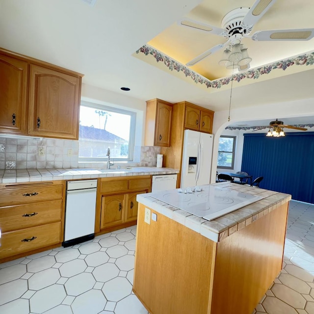 kitchen featuring tile countertops, ceiling fan, backsplash, a tray ceiling, and white fridge with ice dispenser