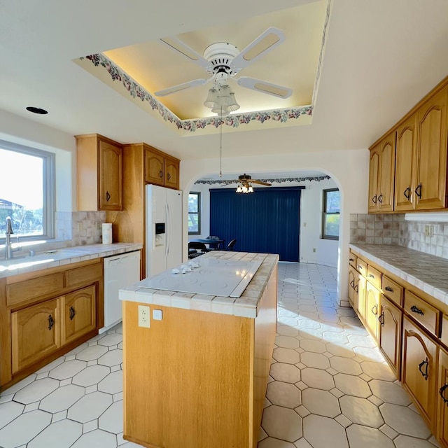 kitchen with white appliances, a tray ceiling, tasteful backsplash, and a kitchen island