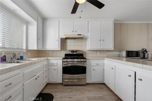 kitchen with under cabinet range hood, tile countertops, appliances with stainless steel finishes, white cabinetry, and a sink