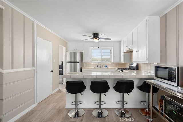 kitchen featuring a peninsula, tile countertops, under cabinet range hood, and stainless steel appliances