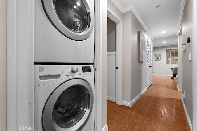 washroom with stacked washing maching and dryer, crown molding, and wood-type flooring