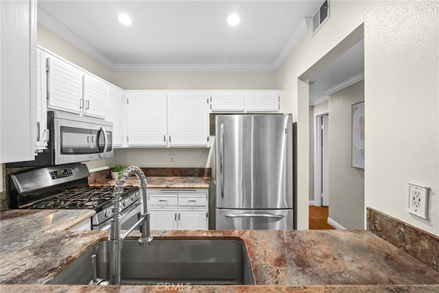 kitchen featuring appliances with stainless steel finishes, dark stone countertops, ornamental molding, and white cabinetry