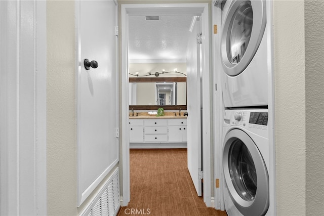 laundry area featuring a textured ceiling, light hardwood / wood-style floors, sink, stacked washing maching and dryer, and ornamental molding