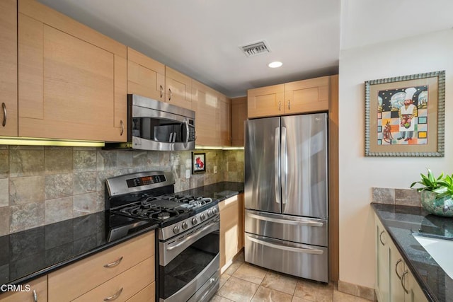 kitchen featuring dark stone countertops, backsplash, light tile patterned floors, stainless steel appliances, and light brown cabinets