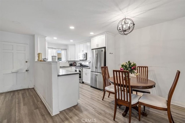 kitchen featuring decorative light fixtures, light hardwood / wood-style floors, kitchen peninsula, white cabinetry, and appliances with stainless steel finishes