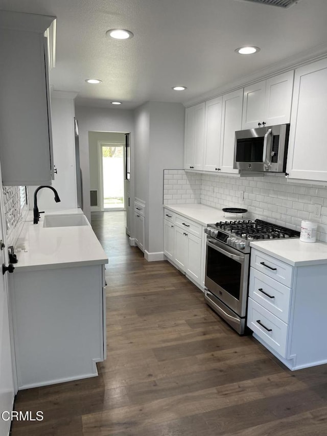 kitchen with appliances with stainless steel finishes, dark hardwood / wood-style floors, backsplash, white cabinets, and sink