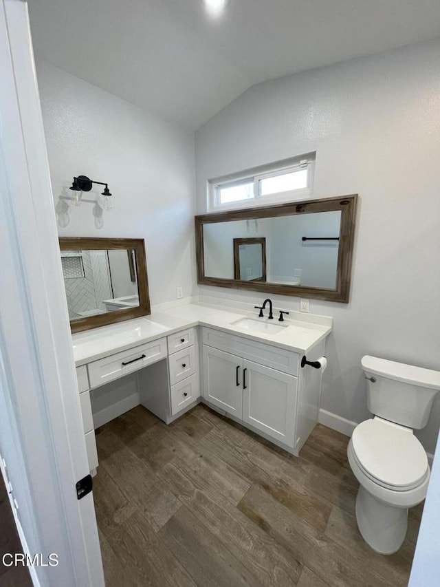 bathroom featuring wood-type flooring, toilet, vanity, and vaulted ceiling