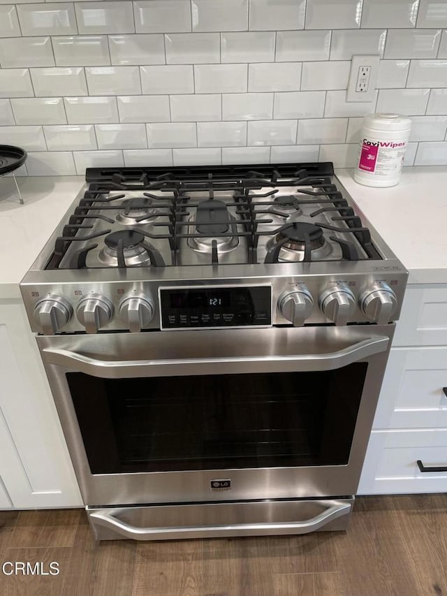 details featuring decorative backsplash, dark hardwood / wood-style floors, stainless steel range with gas stovetop, and white cabinetry