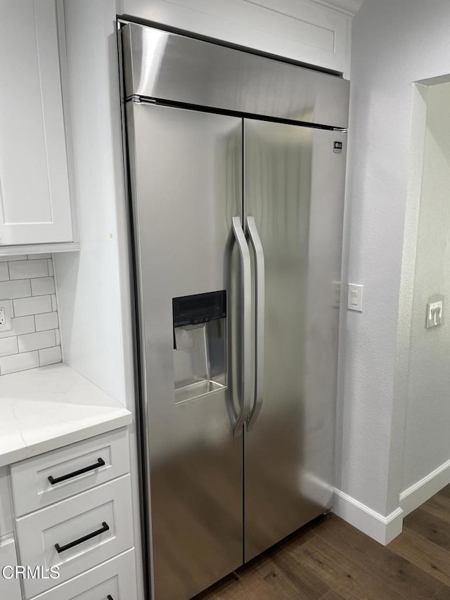 kitchen with tasteful backsplash, dark hardwood / wood-style floors, white cabinetry, light stone countertops, and built in refrigerator