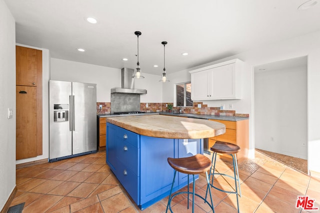 kitchen featuring white cabinets, wall chimney exhaust hood, a kitchen island, stainless steel appliances, and blue cabinets