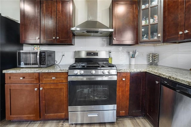 kitchen with tasteful backsplash, appliances with stainless steel finishes, light stone counters, and range hood