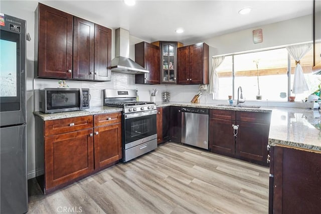 kitchen featuring sink, stainless steel appliances, light stone countertops, wall chimney exhaust hood, and light wood-type flooring