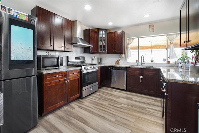 kitchen with appliances with stainless steel finishes, sink, wall chimney range hood, and light stone counters