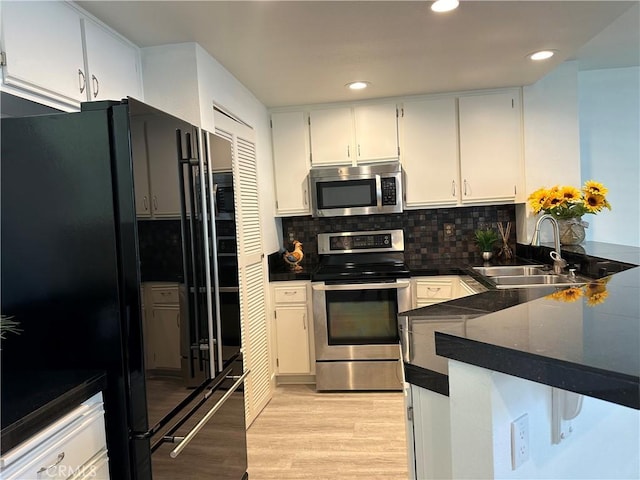 kitchen featuring white cabinetry, stainless steel appliances, light hardwood / wood-style floors, sink, and backsplash