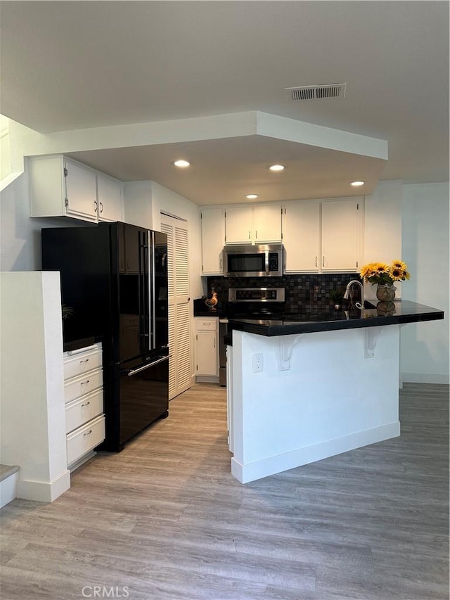 kitchen featuring a kitchen breakfast bar, kitchen peninsula, stainless steel appliances, and white cabinets