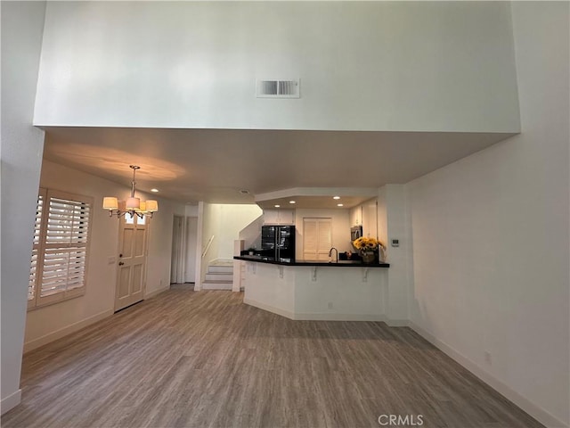 unfurnished living room featuring sink, wood-type flooring, and a notable chandelier