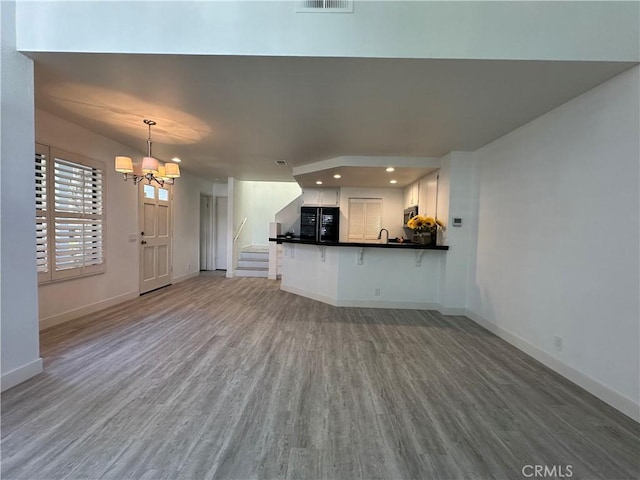 unfurnished living room featuring an inviting chandelier, hardwood / wood-style floors, and sink