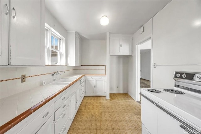 kitchen with sink, white cabinetry, tile countertops, decorative backsplash, and stove