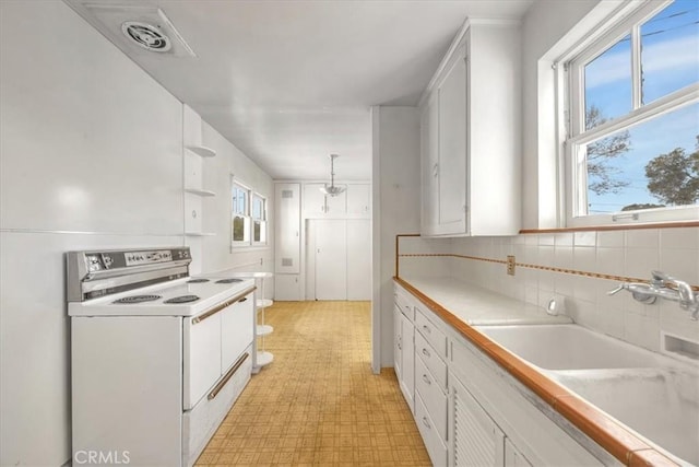 kitchen with white cabinetry, sink, decorative light fixtures, and white electric range oven