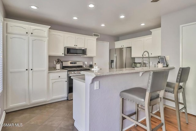 kitchen with stainless steel appliances, light stone countertops, white cabinets, a kitchen bar, and kitchen peninsula