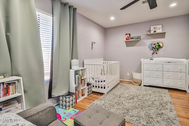 bedroom featuring light hardwood / wood-style floors, a nursery area, and ceiling fan