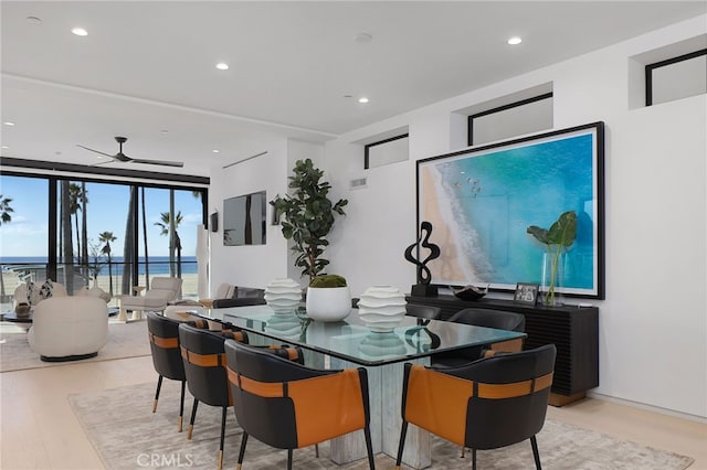 dining area featuring a water view, ceiling fan, expansive windows, and light hardwood / wood-style flooring