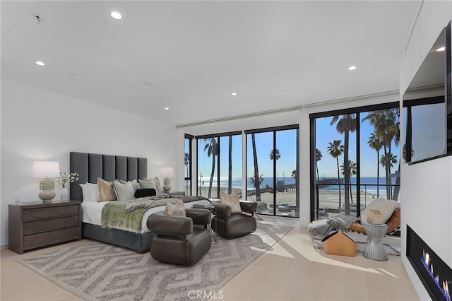 bedroom featuring expansive windows, a water view, access to outside, and light hardwood / wood-style flooring