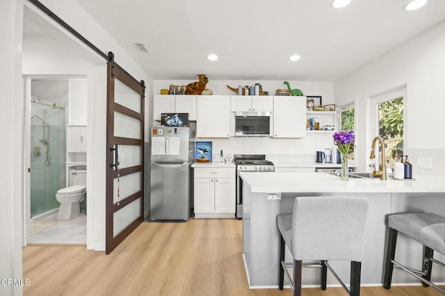 kitchen featuring appliances with stainless steel finishes, a barn door, a kitchen bar, and white cabinets