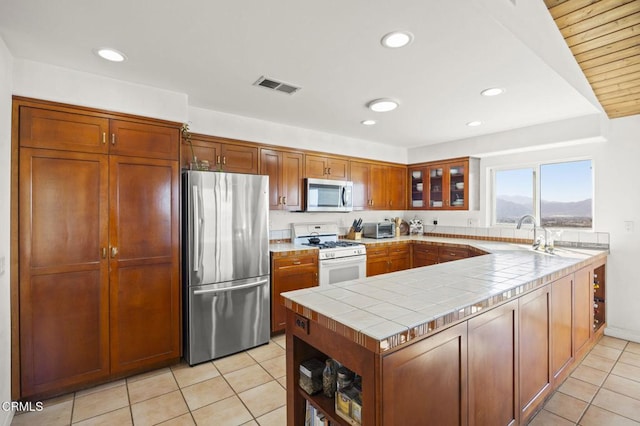 kitchen with sink, tile countertops, light tile patterned floors, kitchen peninsula, and stainless steel appliances