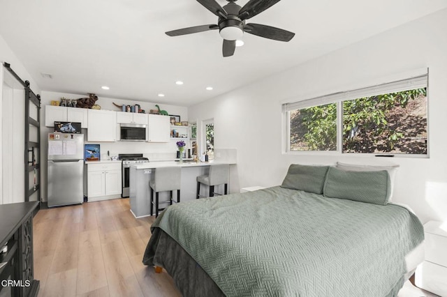 bedroom with ceiling fan, a barn door, stainless steel refrigerator, and light hardwood / wood-style floors