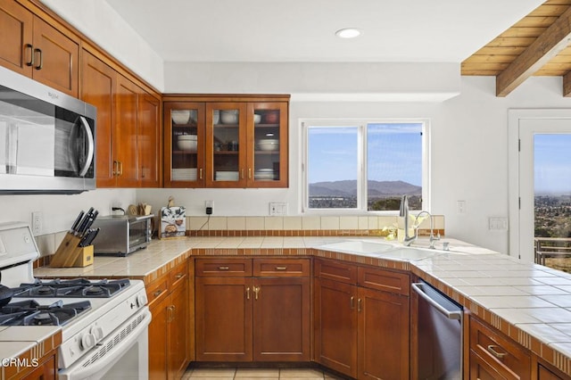 kitchen with stainless steel appliances, tile countertops, a mountain view, and sink