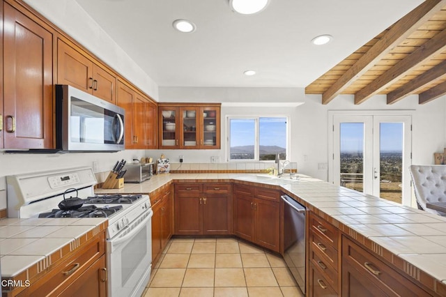 kitchen featuring tile countertops, stainless steel appliances, glass insert cabinets, light tile patterned flooring, and a sink