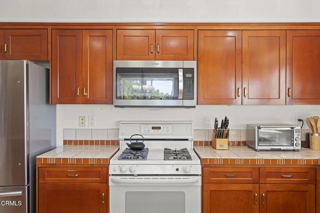 kitchen featuring stainless steel appliances, tile counters, brown cabinets, and a toaster