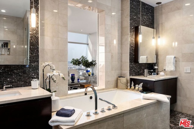 bathroom featuring tiled bath, vanity, and tile walls