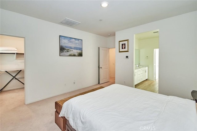 bedroom with ensuite bath, a spacious closet, and light carpet