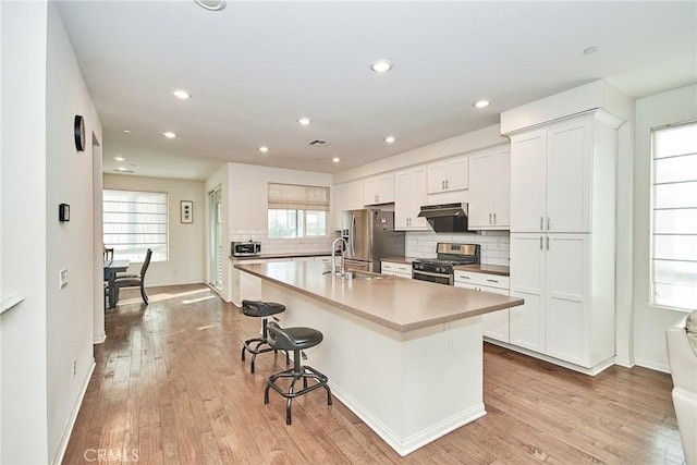 kitchen with white cabinetry, stainless steel appliances, a kitchen island with sink, and light wood-type flooring