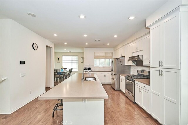 kitchen featuring white cabinets, appliances with stainless steel finishes, a kitchen breakfast bar, sink, and a center island with sink