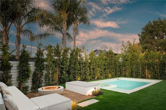 pool at dusk featuring a fire pit and a lawn